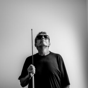Ein schwarz weiß Foto von einem blinden Mann der einen Blindenstock hält.