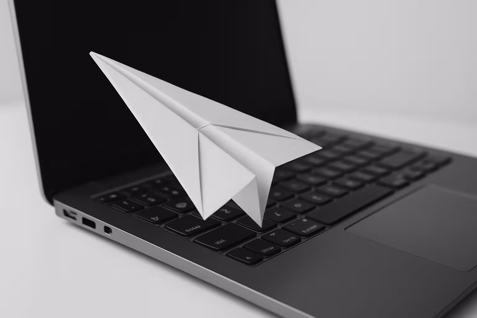 Ein schwarz weiß Foto von einem Laptop und einem Papierflieger.